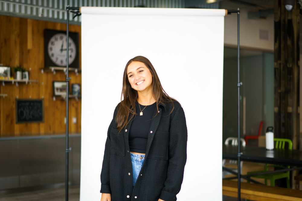 a smiling person standing in front of a white backdrop