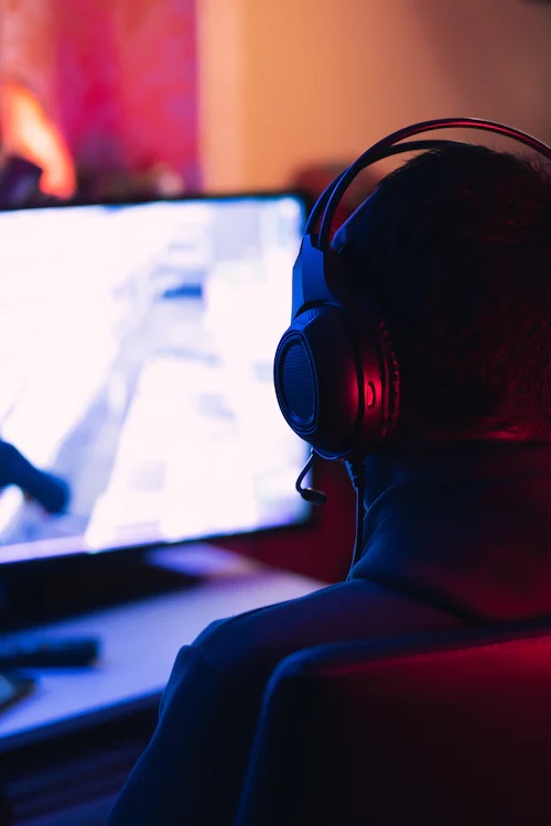 A person with a headset playing a video game on their laptop